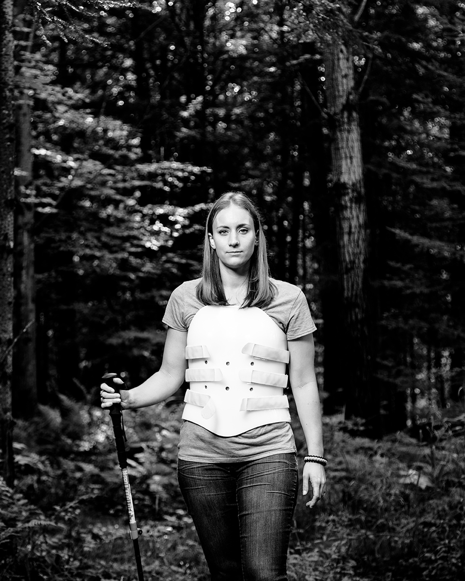 editorial photographer Midwest - Amber Kohnhorst stands in the woods with a hiking pole, wearing a back brace