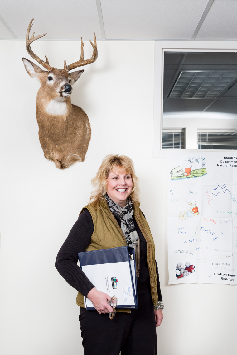 editorial portrait photographer - Cathy Stepp stands in her office below a taxidermy deer head