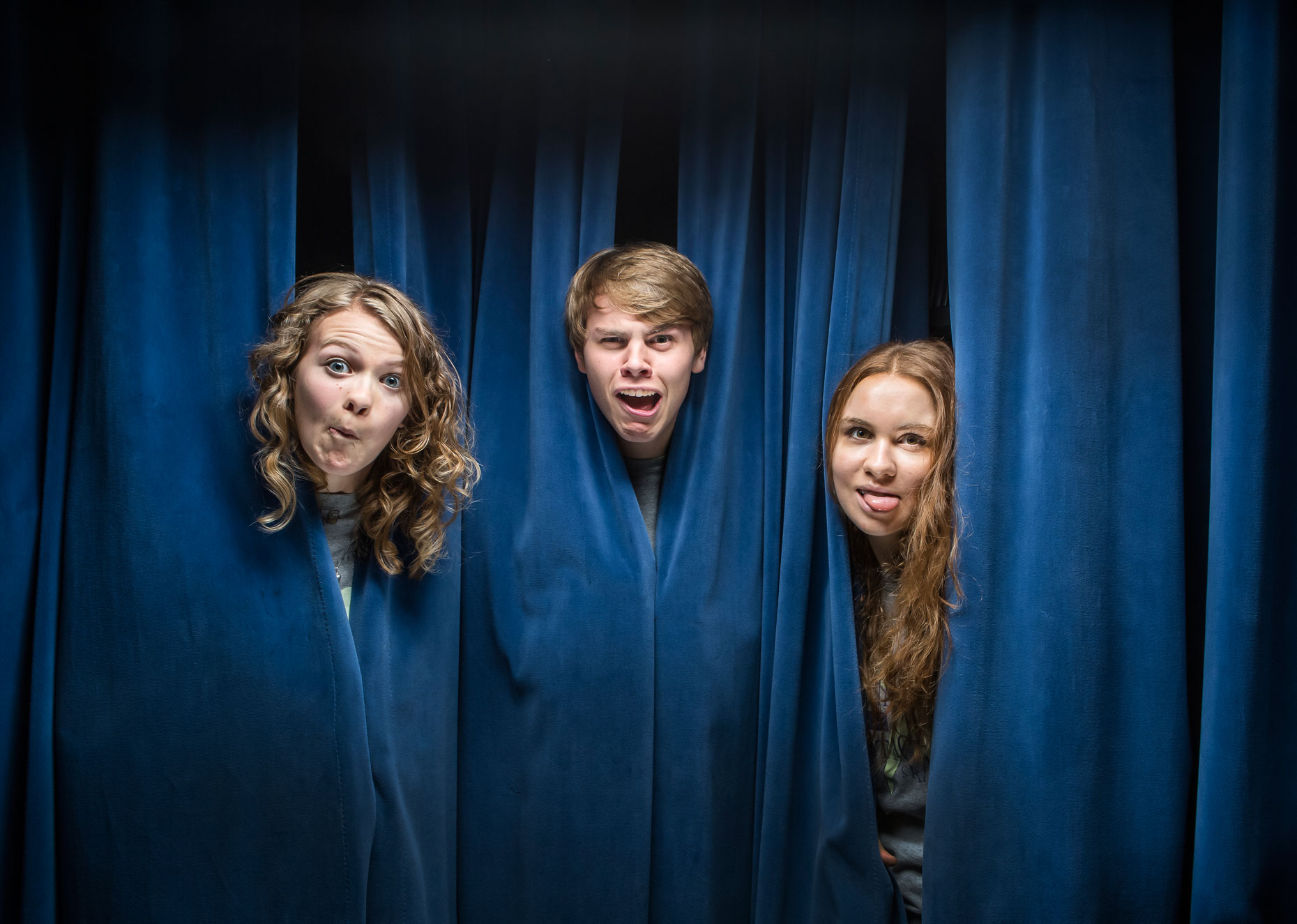 editorial photographer Milwaukee - young actors make silly faces through a blue stage curtain