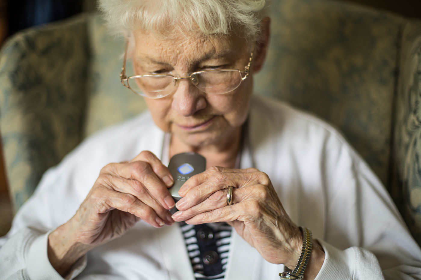 healthcare photographer - an elderly woman tests a life alert device that hands around her neck
