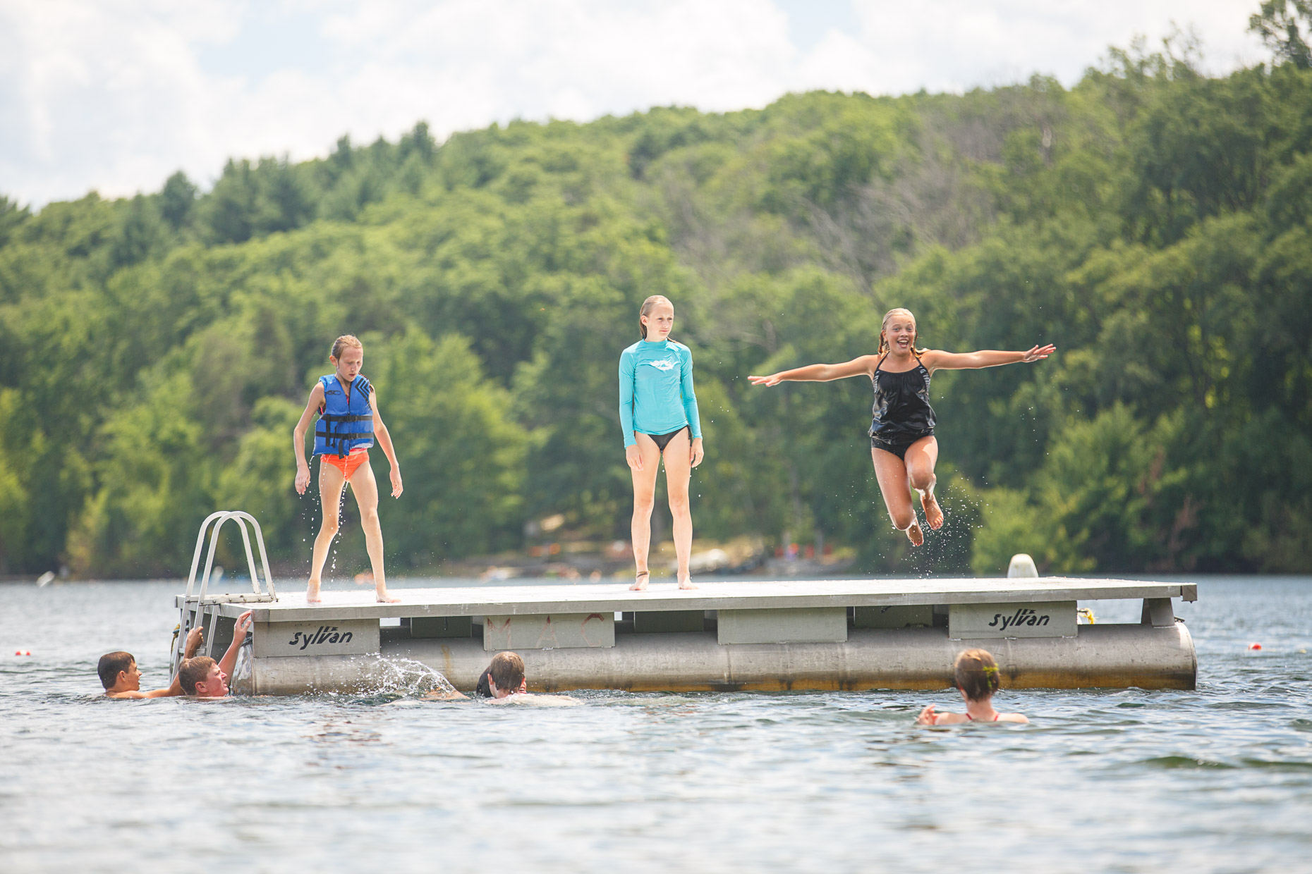commercial photographer Wisconsin - young kids play on a swimming raft in a lake at summer camp